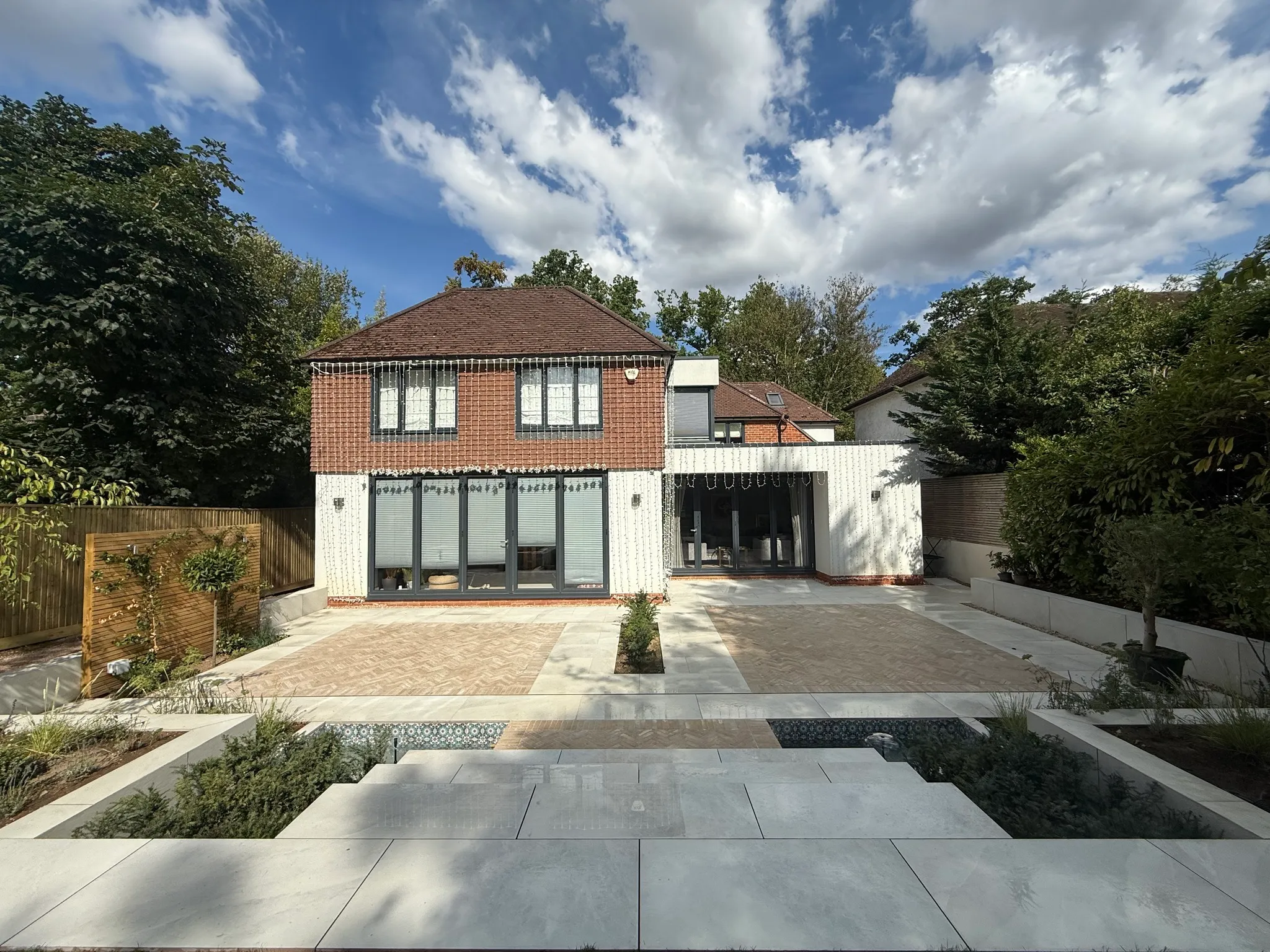 Large porcelain and herringbone brick patio with raised planting beds behind a detached house