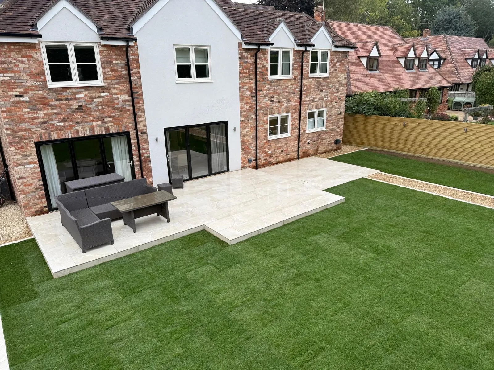 Cream porcelain patio with garden furniture beside a new lawn at the back of a brick house
