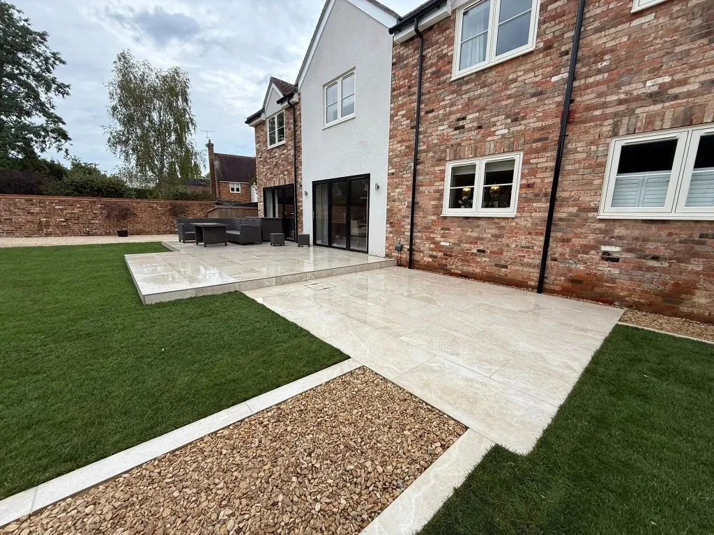 Porcelain patio and seating area at the back of a brick house, with a new lawn and gravel path